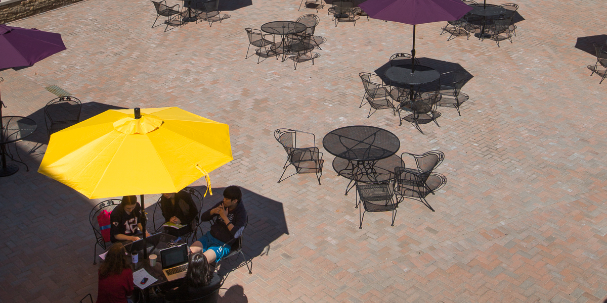 Students gather under a yellow umbrella on the Gizmo Patio.
