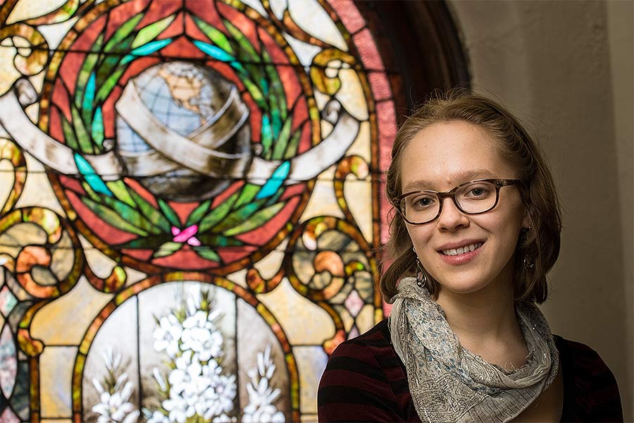 Knox College student Sophia Croll, in front of a memorial stained glass window that includes a globe, in a church near campus.